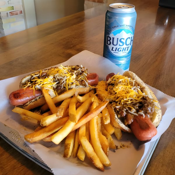 Two chili cheese dogs with fries and a Busch Light beer on a wooden table.