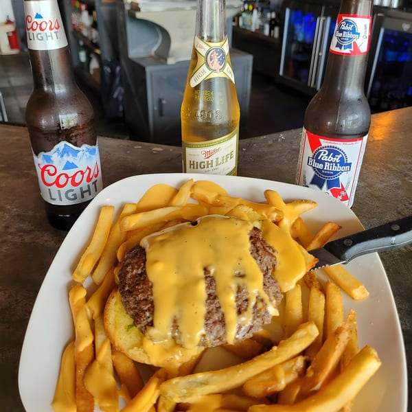 Cheeseburger and fries covered in cheese sauce, with three beer bottles on a bar top.